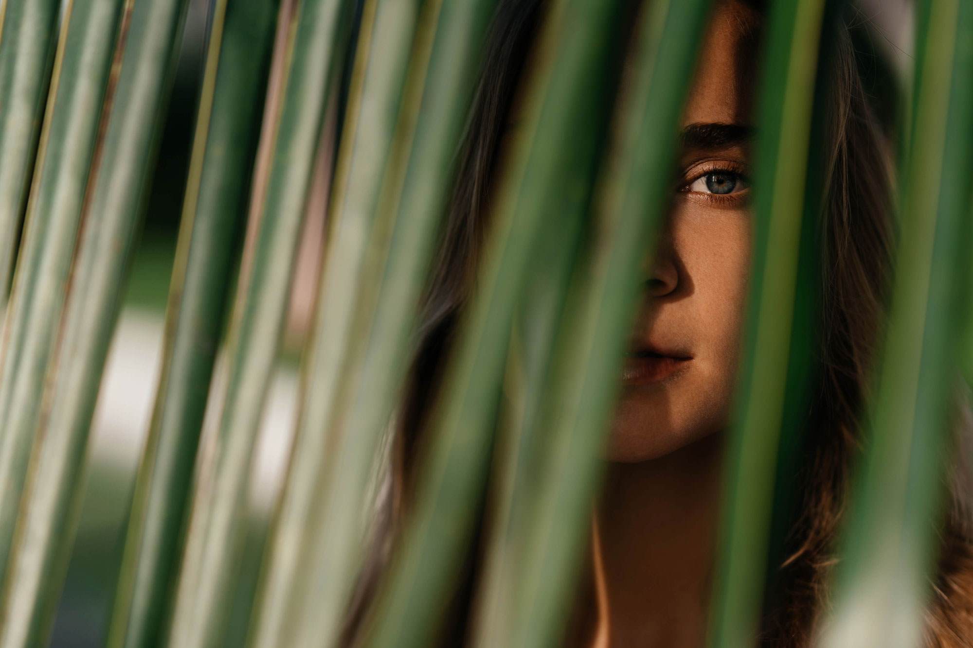 Women peaking though green plant with sun reflection