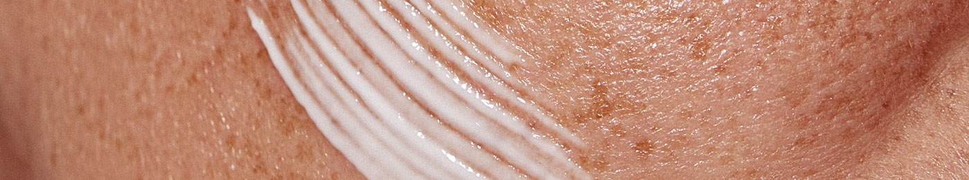 Close up on a  white woman's freckled face with serum smeared across it
