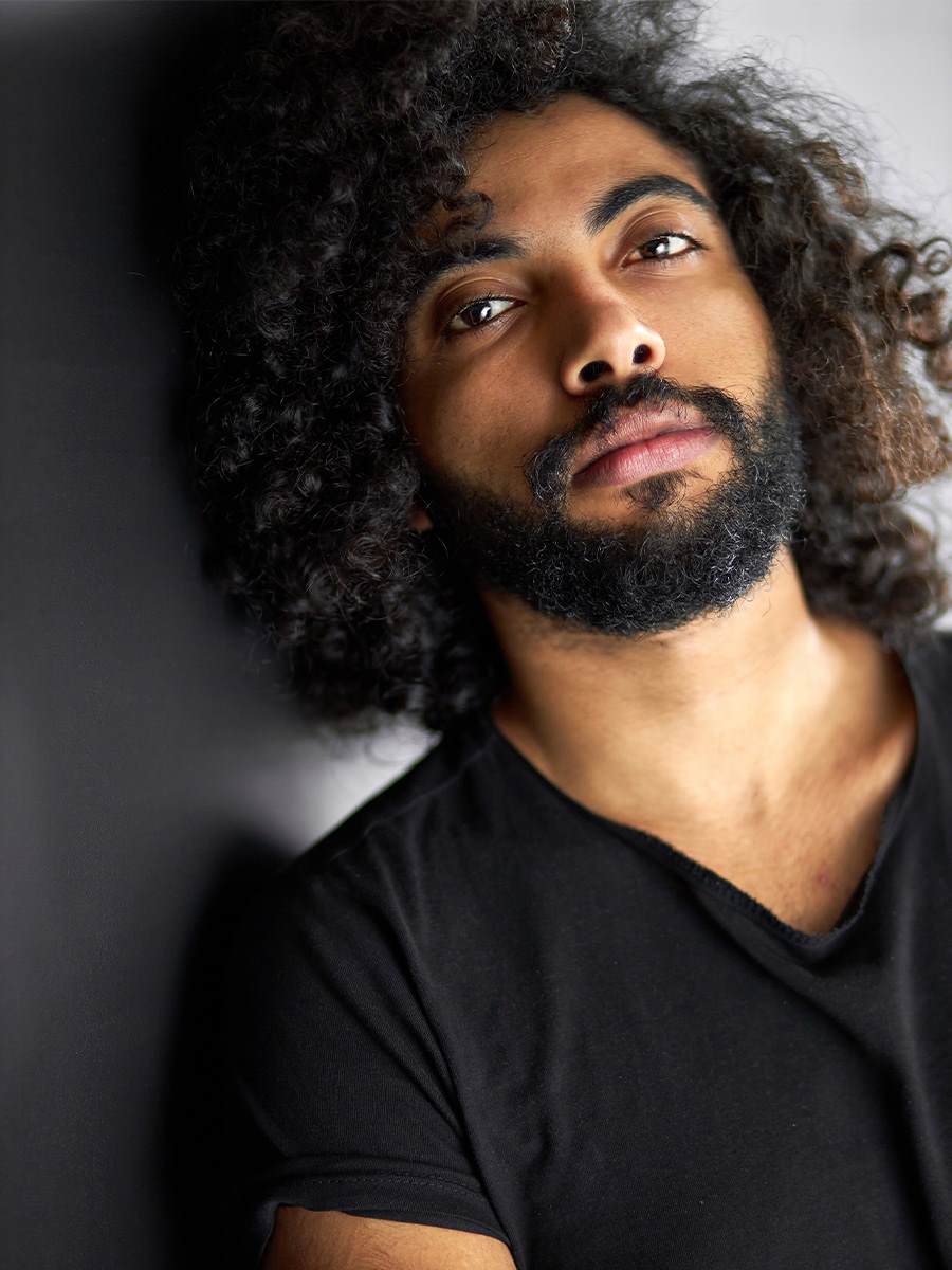 Middle eastern man with beard and curly hair staring at the camera.