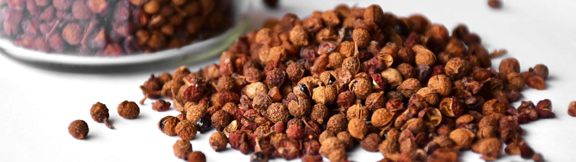 A pile of Sichuan pepper corns (small brownish red pepper corns) against a white background.