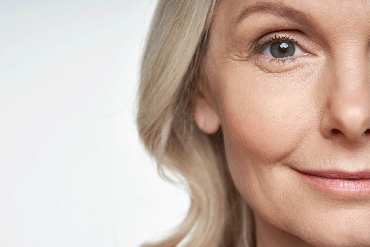 A photo of the right half of a woman's face. She is looking directly at the camera and smiling. She's older, maybe 50 or 60. She is smiling warmly.