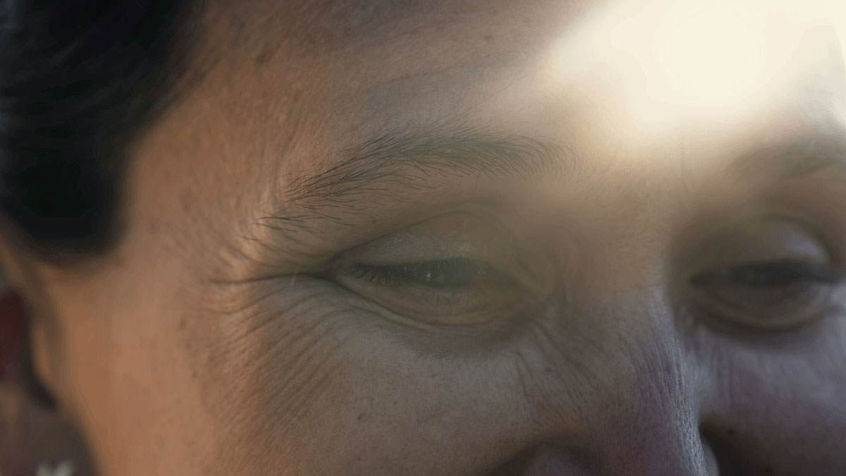 Close up on A photo of just the area around the eyes of an older Asian woman. She has noticeable wrinkles but a genuine smile in her eyes. There is a strong lens flare indicating this is a sunny day.