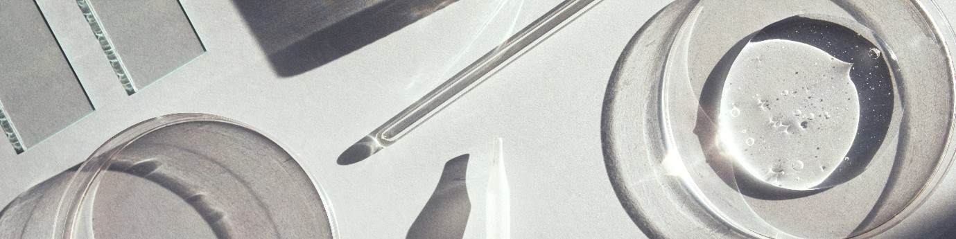 Cropped image of various pieces of lab equipment, petri dishes, glass droppers, slides, etc. They are arranged on a grey background.