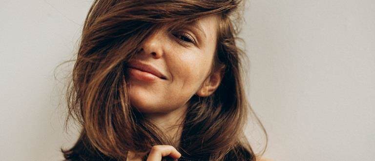 Young white woman with long brown straight hair. She is smiling at the camera. Her hair is flipped over her head covering one eye.