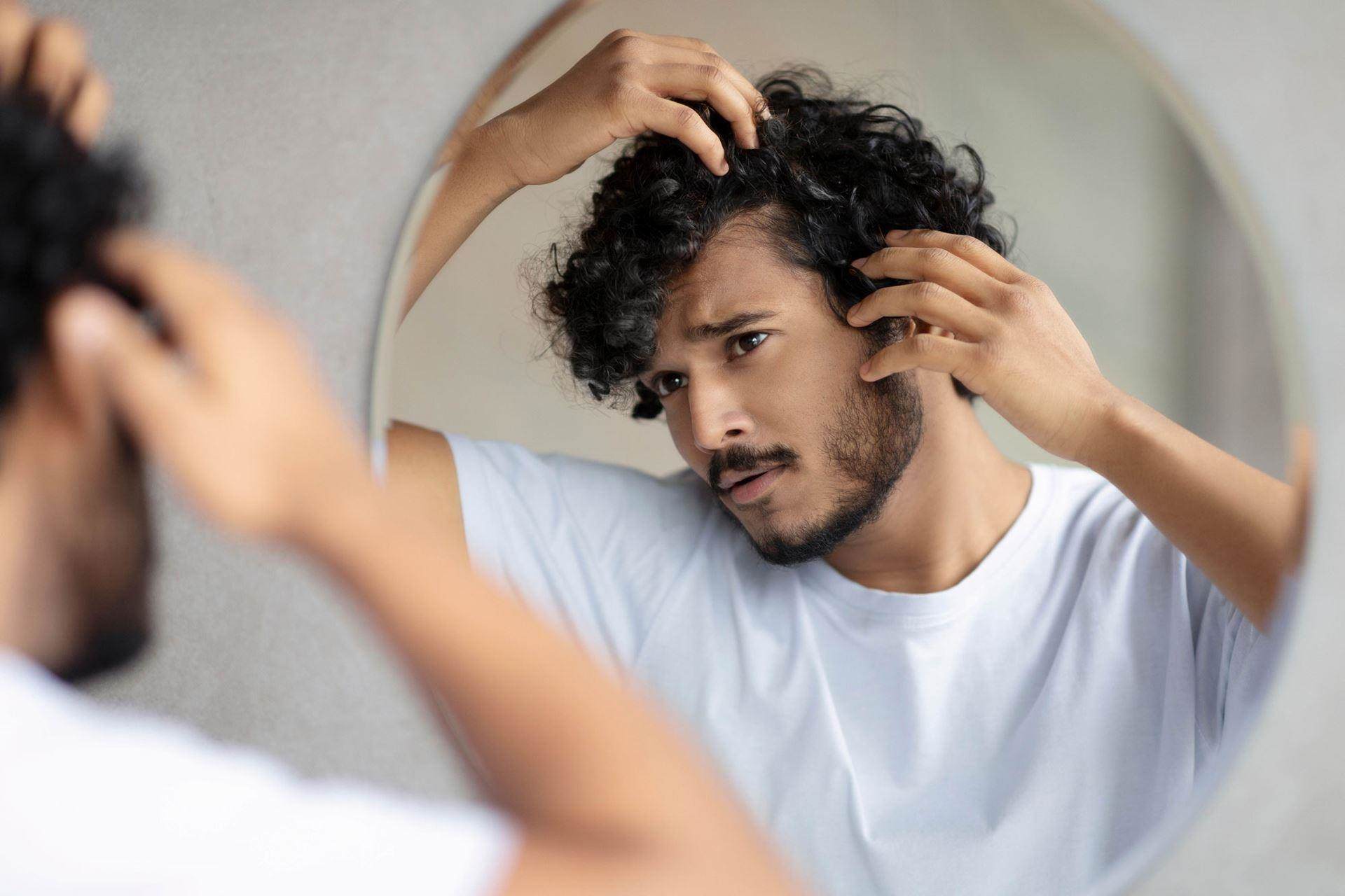 a man looking in the mirror and holding his hair