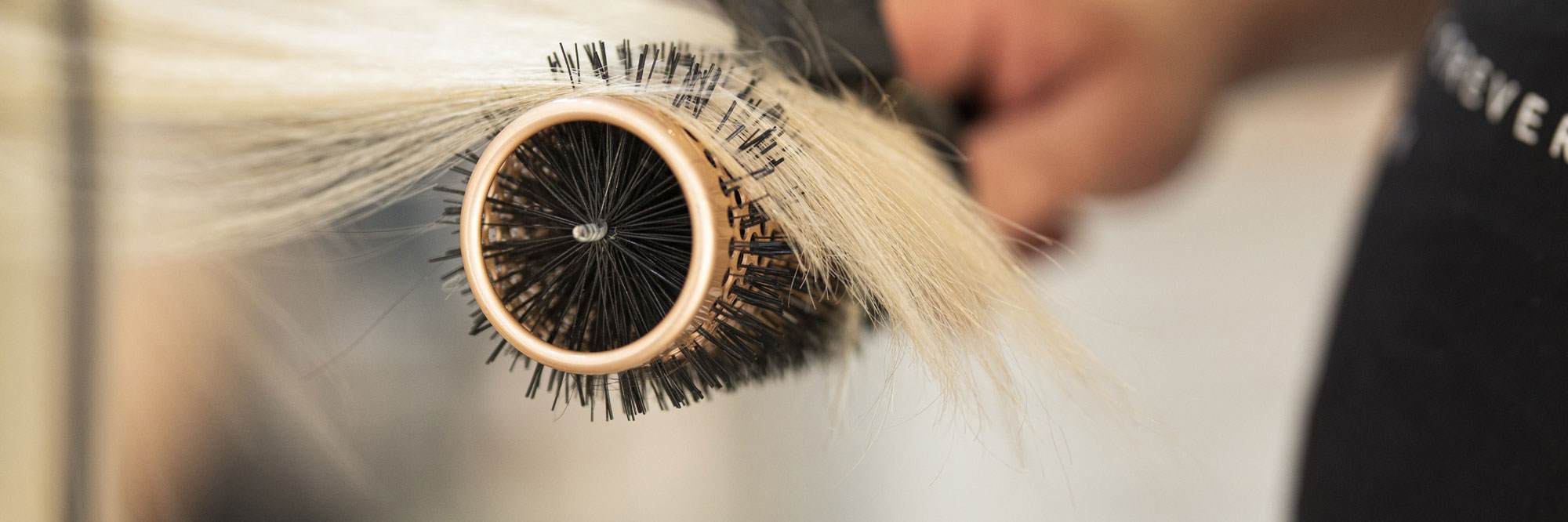 Cropped image of a curling brush and hair dryer curling the ends of some frizzy blonde hair