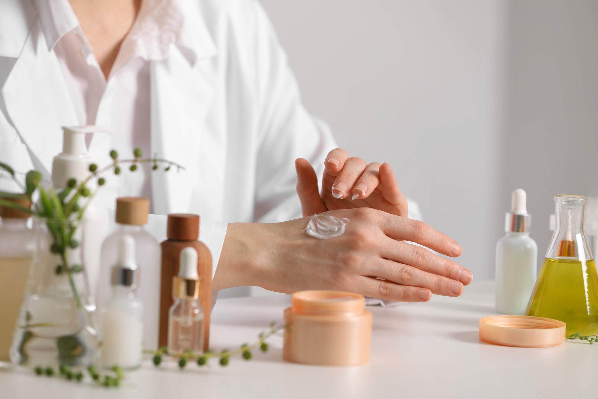 Formulator applying white cream to hands with examples of beauty products around them