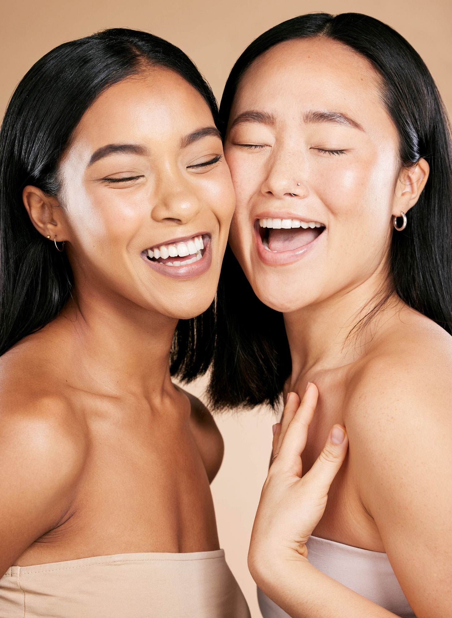 Two women smiling and embracing joyfully, showcasing natural beauty and healthy skin
