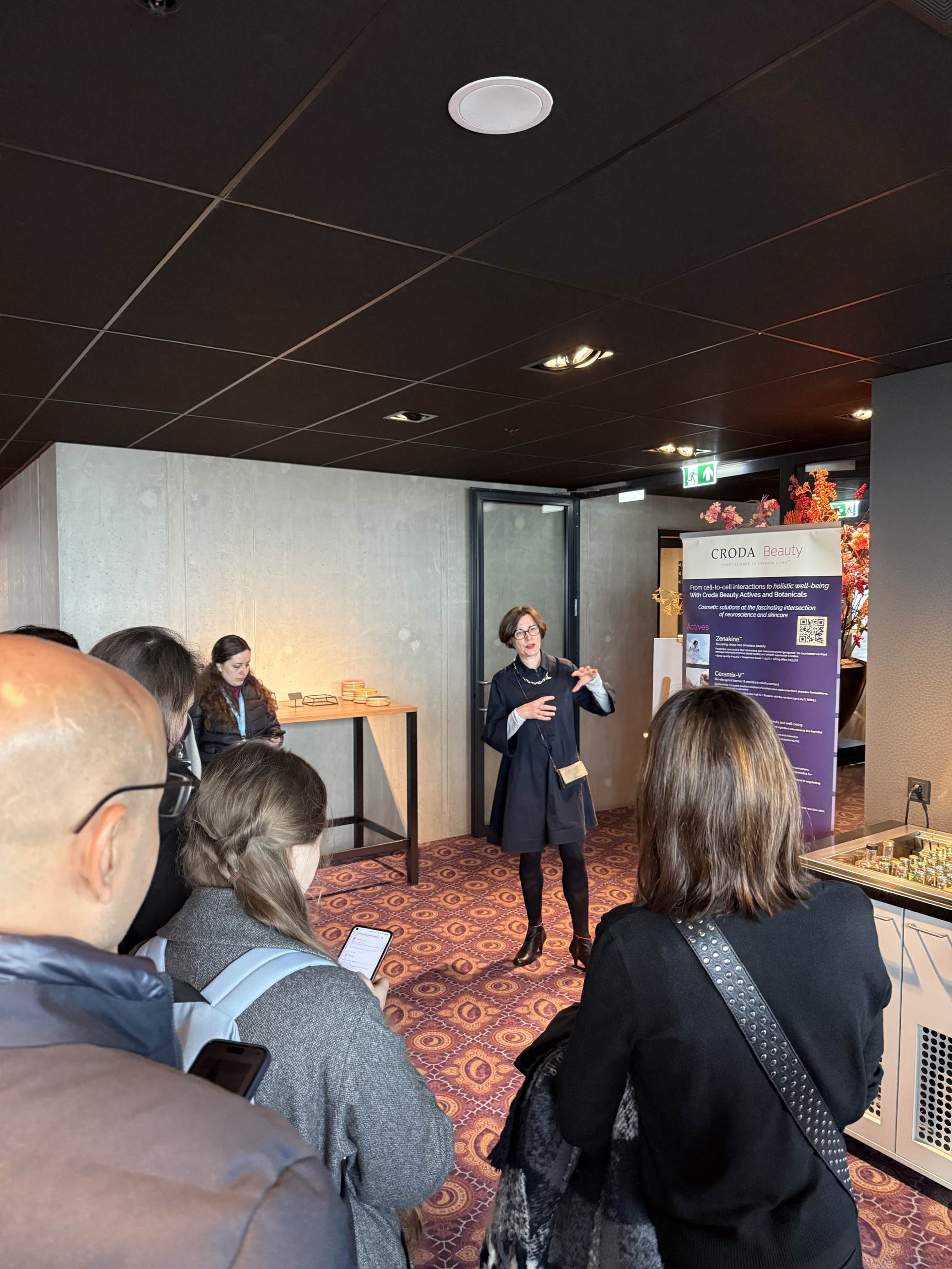 Pascale Rossi delivering a workshop at in-cosmetics global 2025. You can see some of the workshop particpants looking at her. Pascale is a middle aged white woman with short brown hair. 