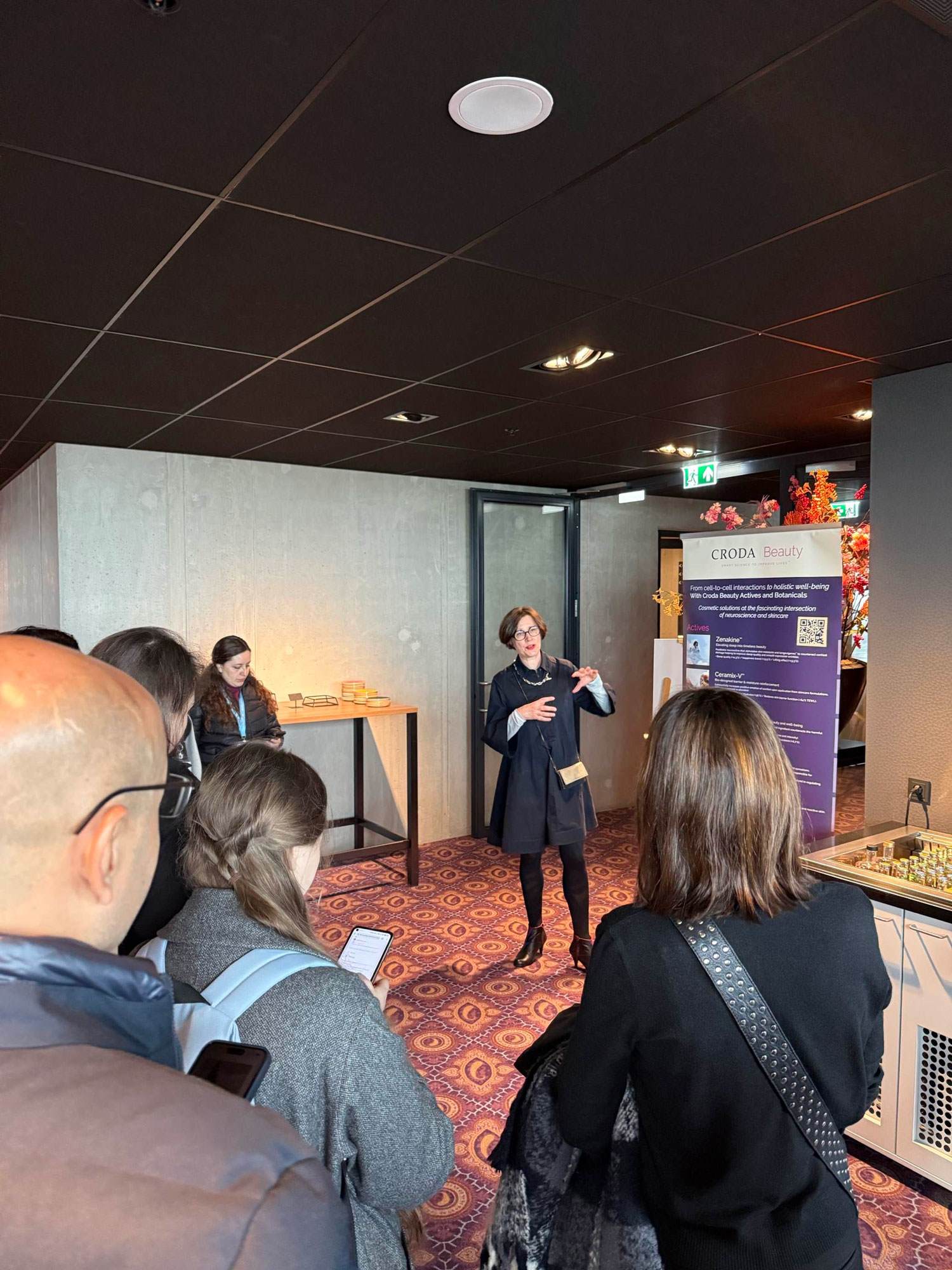 Pascale Rossi delivering a workshop at in-cosmetics global 2025. You can see some of the workshop particpants looking at her. Pascale is a middle aged white woman with short brown hair. 