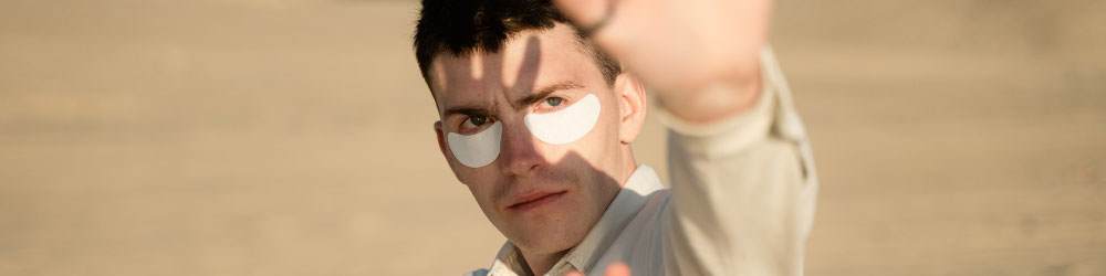 man wearing sun protection patches and holding hands up to the sun to shield his face from the sun light