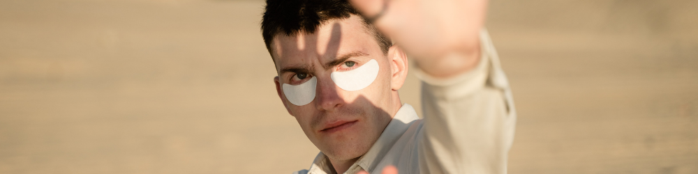 man wearing sun protection patches and holding hands up to the sun to shield his face from the sun light