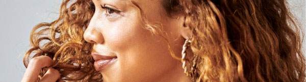 Woman with brown skin and hair smelling her own hair.