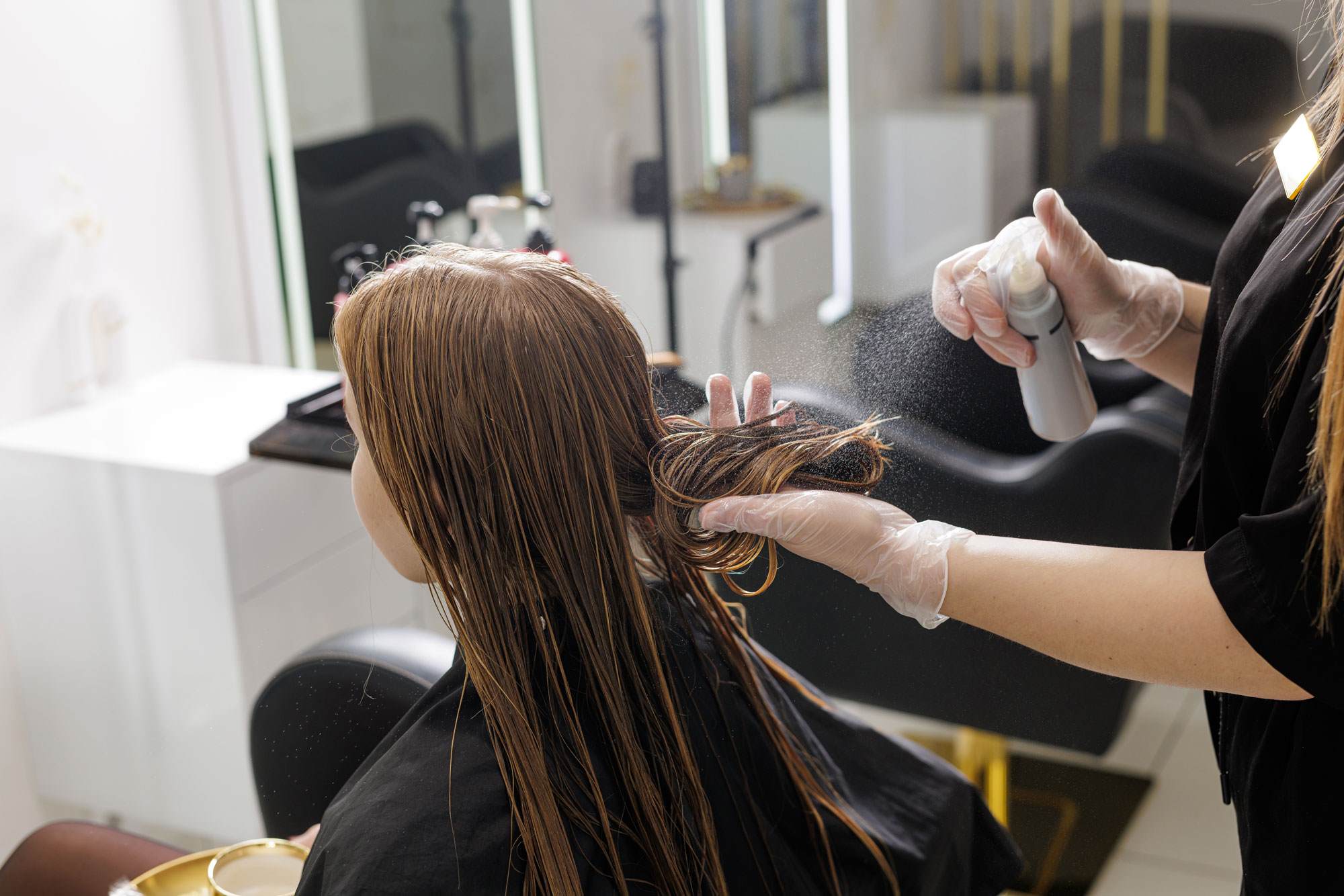 White woman with brown hair in a salon. You can see the hairdresser spraying her hair with a k31 pro mist.