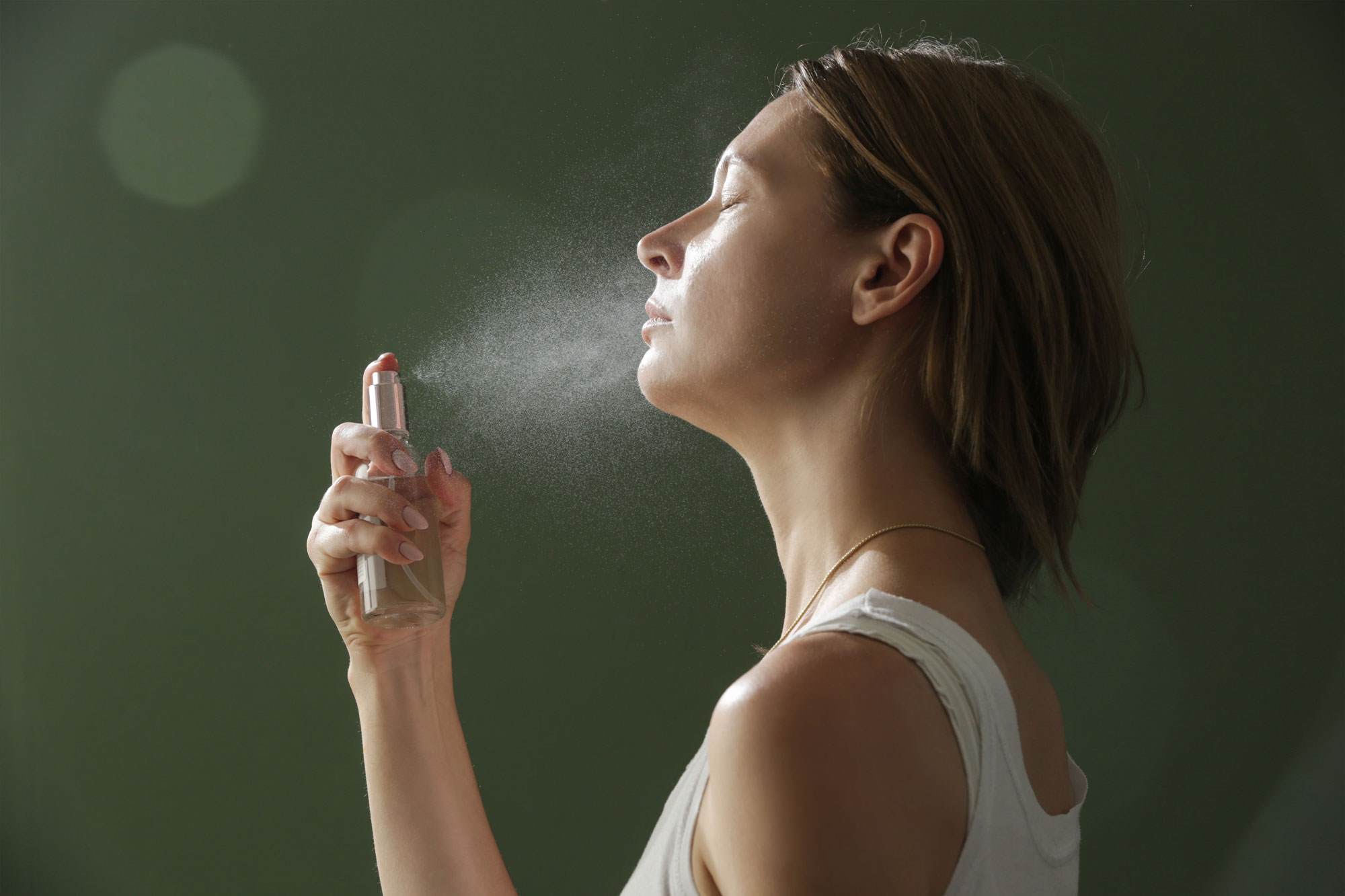 White woman with blonde hair spraying her face with the ultimate glow mist.