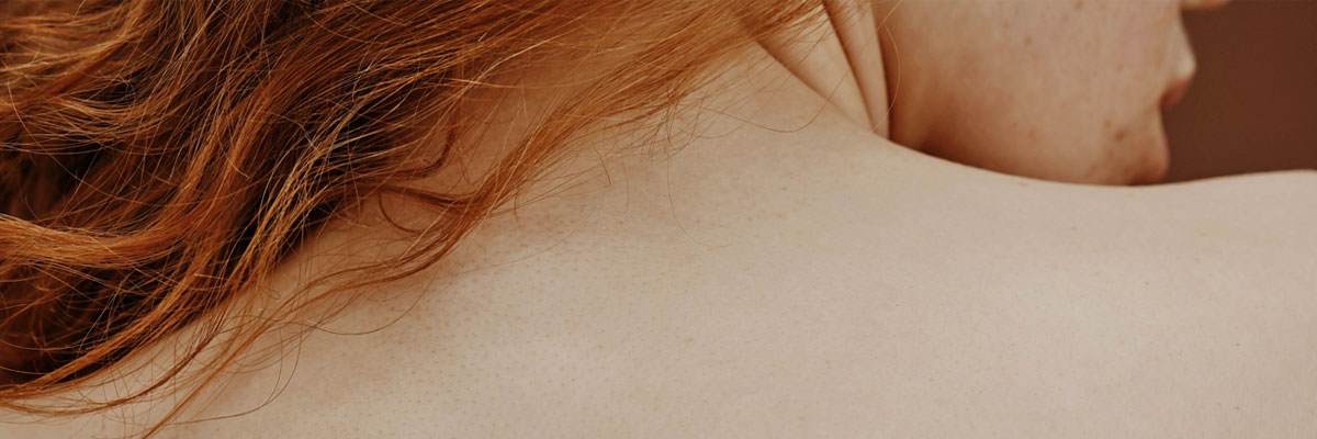 Photo of a red haired woman with white skin's back. You can see a lot of her skin which is flawless. She is looking off to the side but you cannot see most of her face.