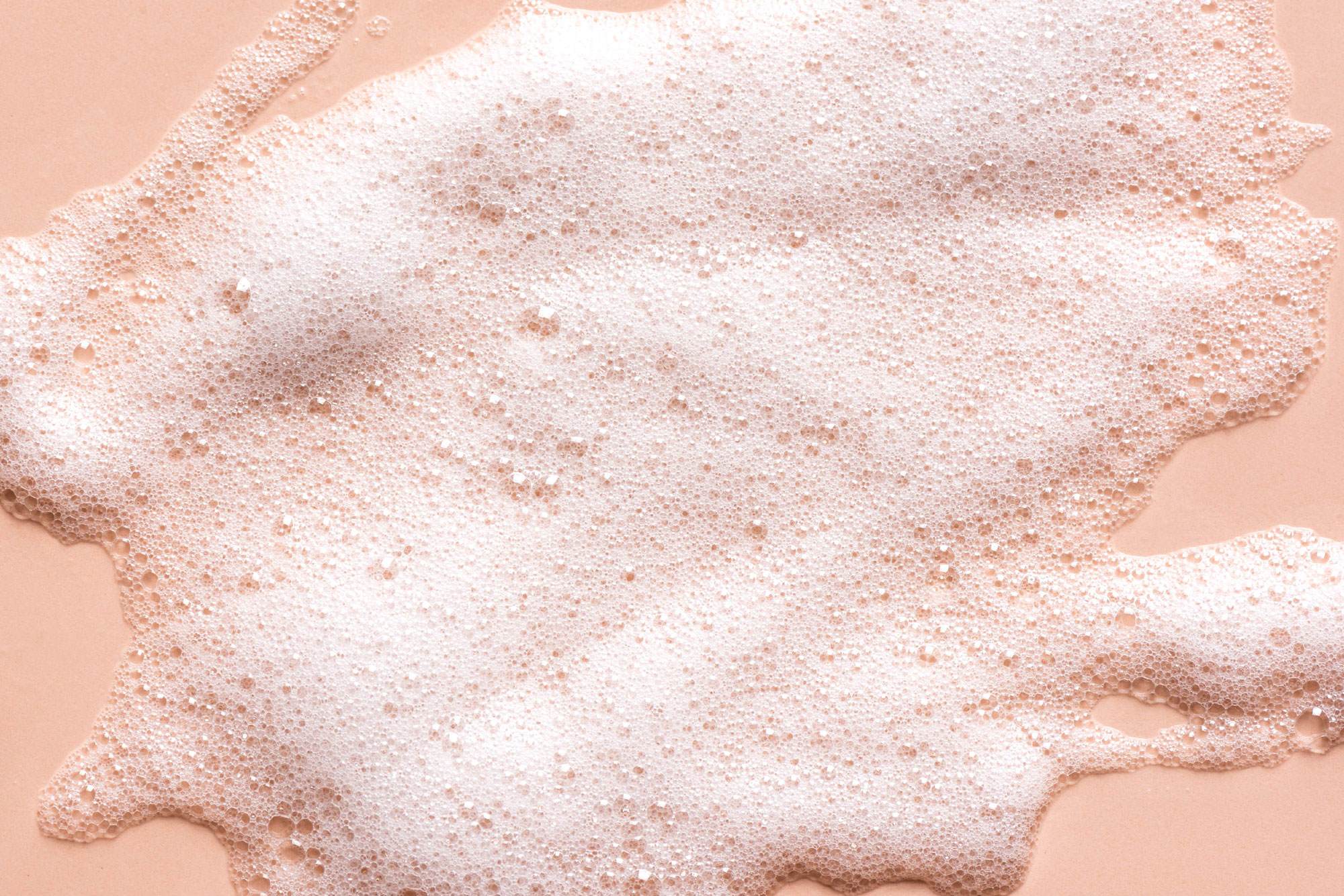 White foaming cleanser bubbles against a peach background