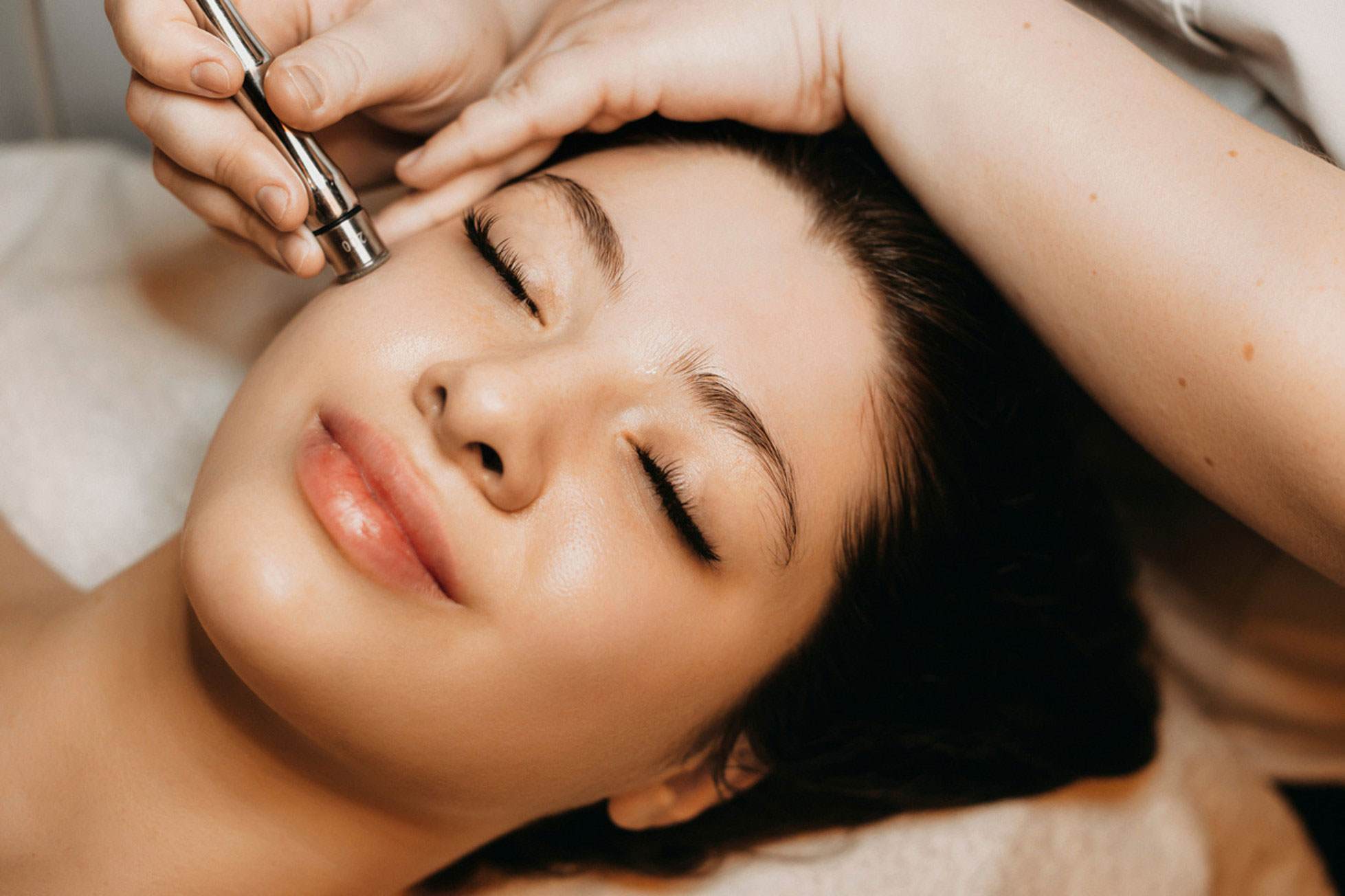 Young white woman smiling with her eyes closed as she receives microneedling treatment