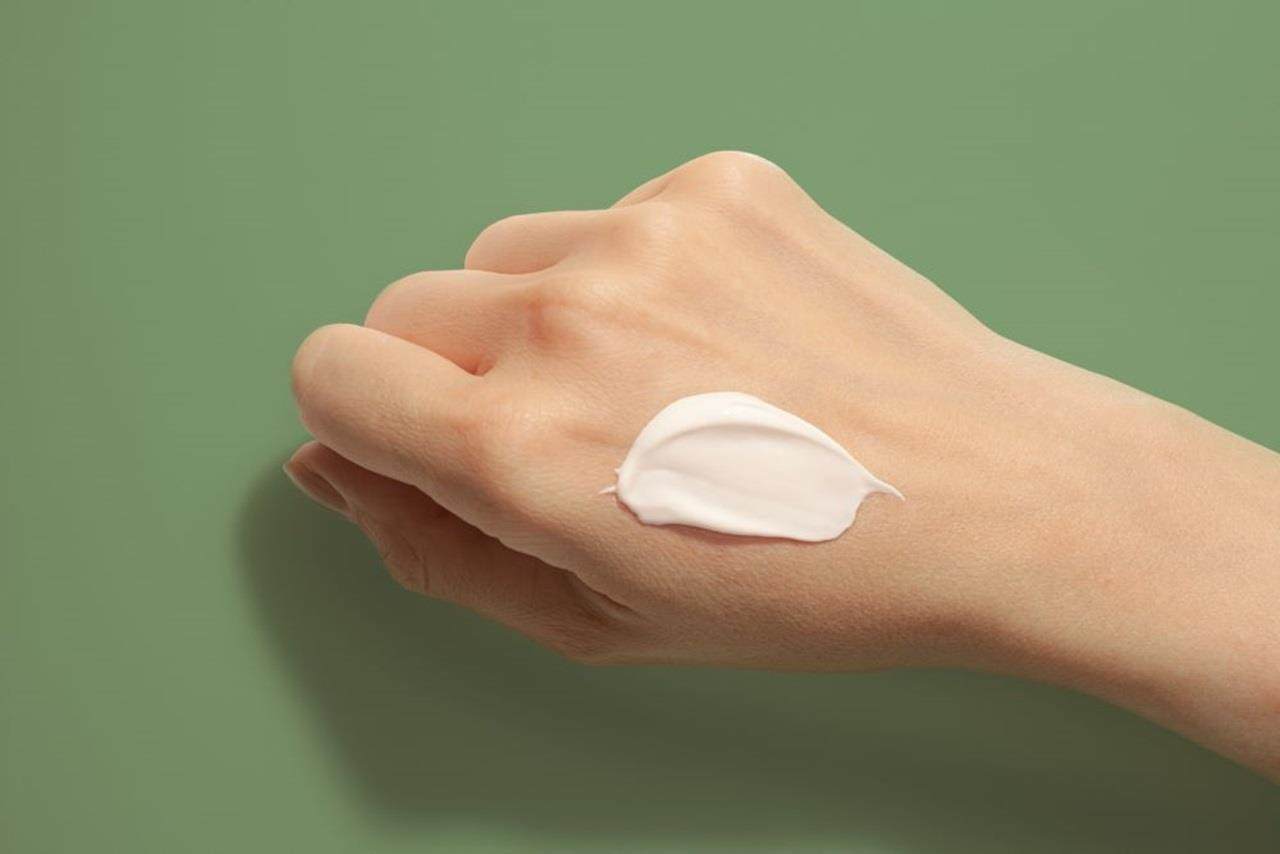 An image of someone's right hand and forearm with white skin over a green background. A dose of a thick, white skin cream has been applied but not yet rubbed into the skin.