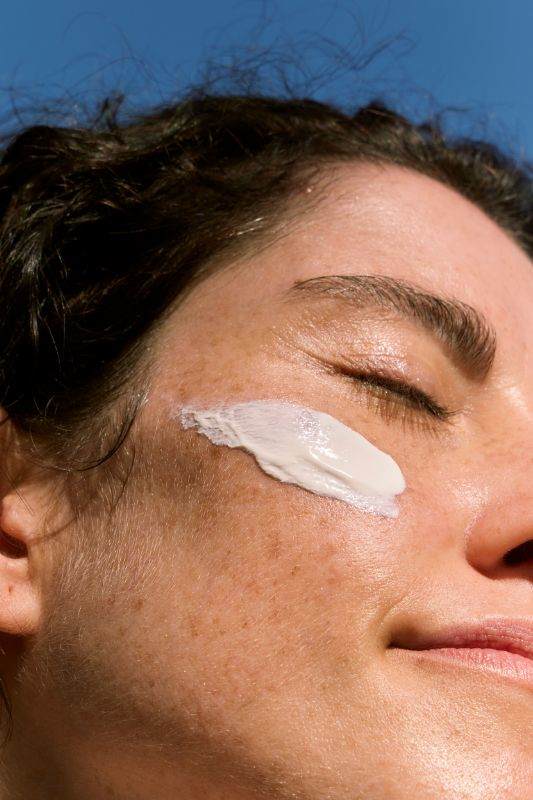 Close-up of woman applying sunscreen to her cheek in sunlight, representing sunscreen formulation and SPF boosters designed for high-performance sun protection