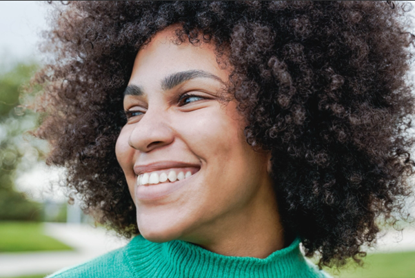One black woman who appears to be in her 20s with large natural hair looking to the left and smiling