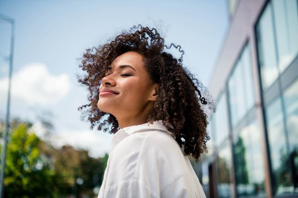 Woman with brown skin and dark brown curly hair smiling in the sunshine