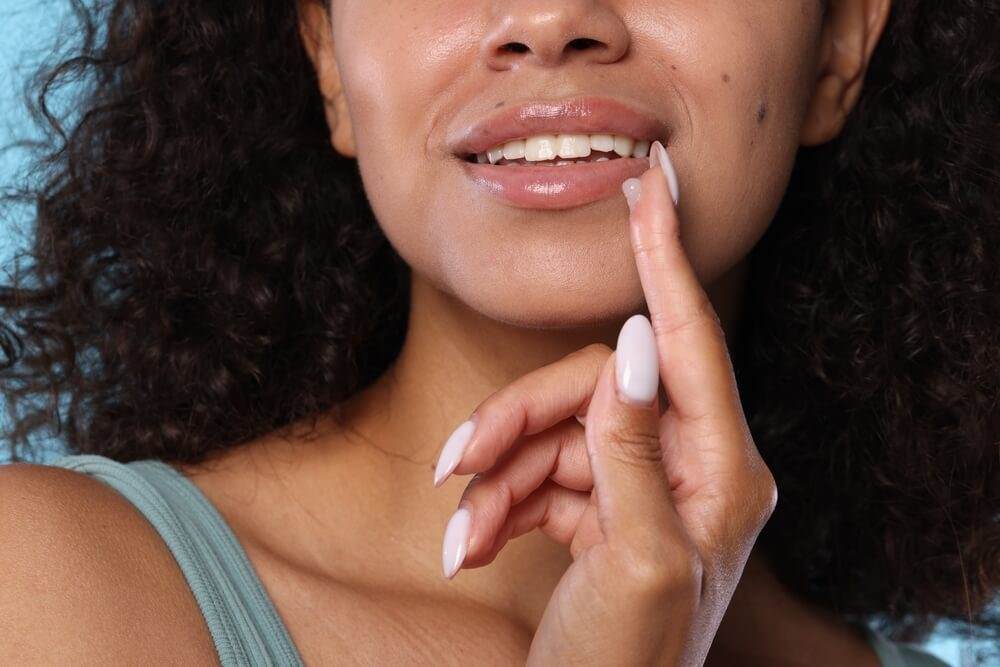 Cropped image of a young woman with brown skin and black curly hair touching her face