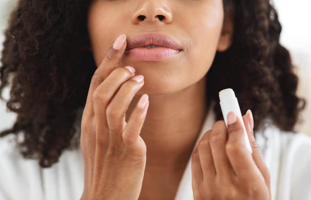 Cropped photo of a young black woman with brown curly hair applying lip balm
