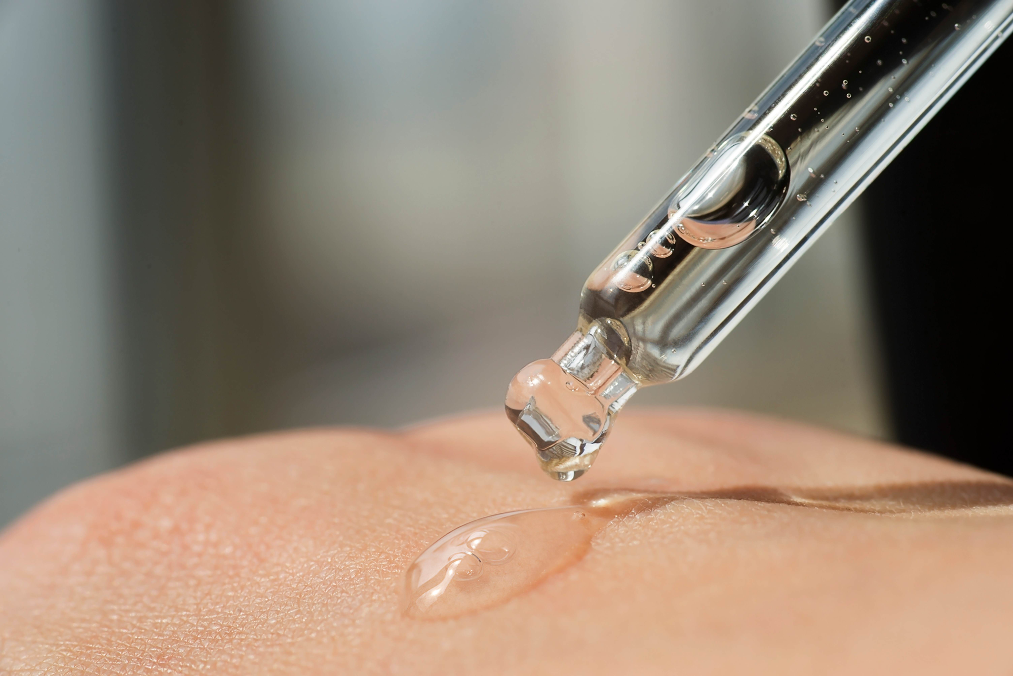 Close-up on pixel perfect serum being dropped onto the back of a White woman's hand.