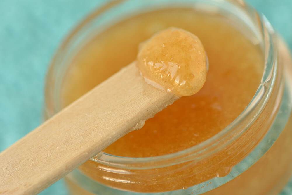 Close up on a wooden lollipop stick dipped into a jar of lip balm scrub