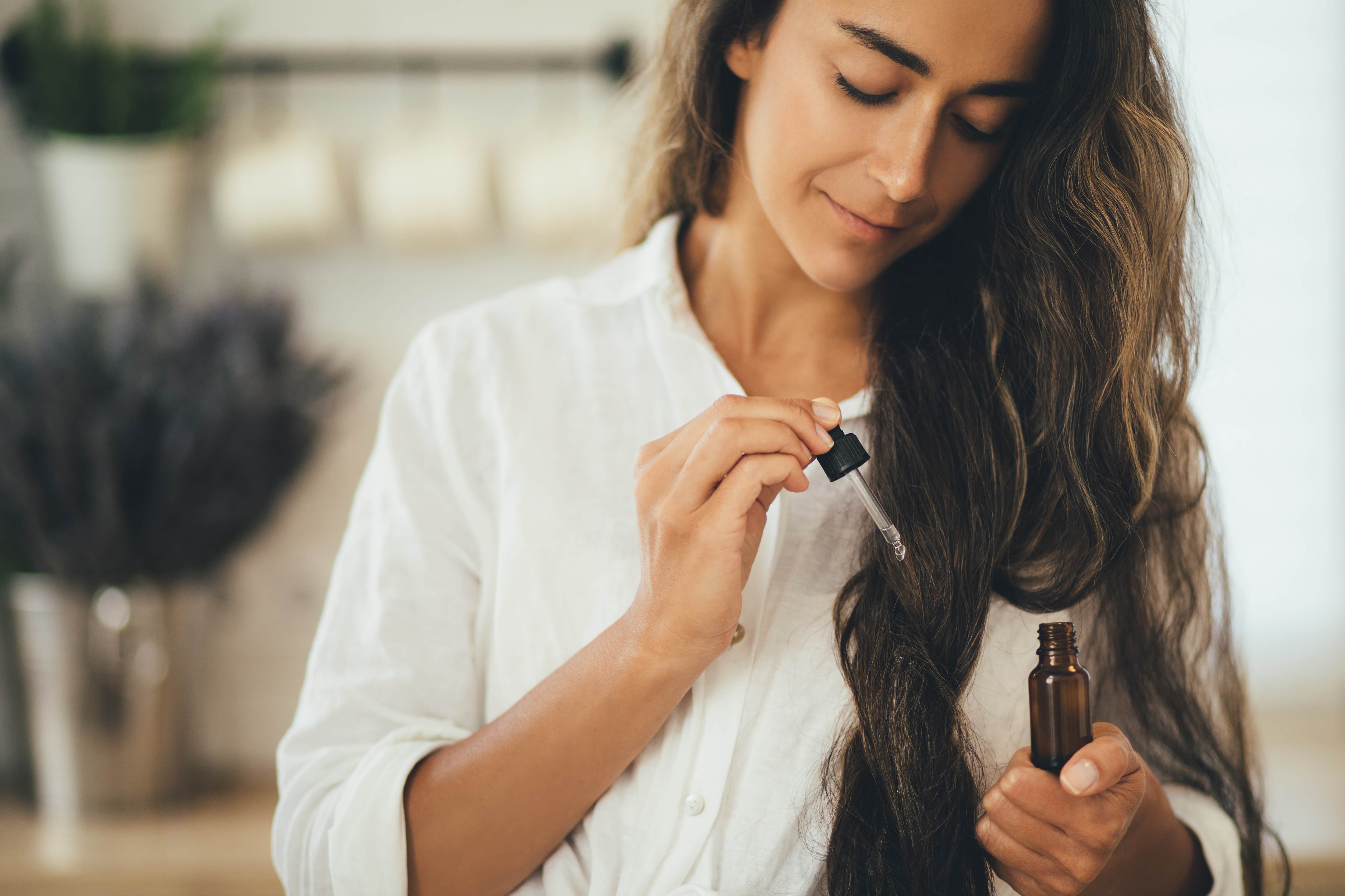 Middle Eastern woman with long brown wavy hair applying a hair magic potion serum to her hair.