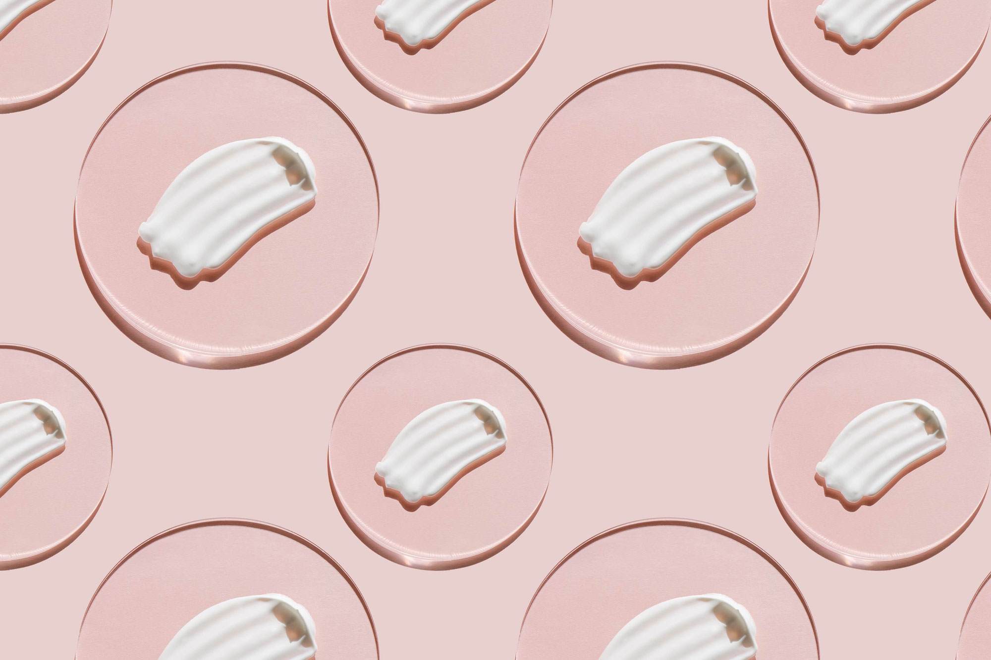 Repeating pattern of a white milky cream smear on a circular oil drop against a pink background.