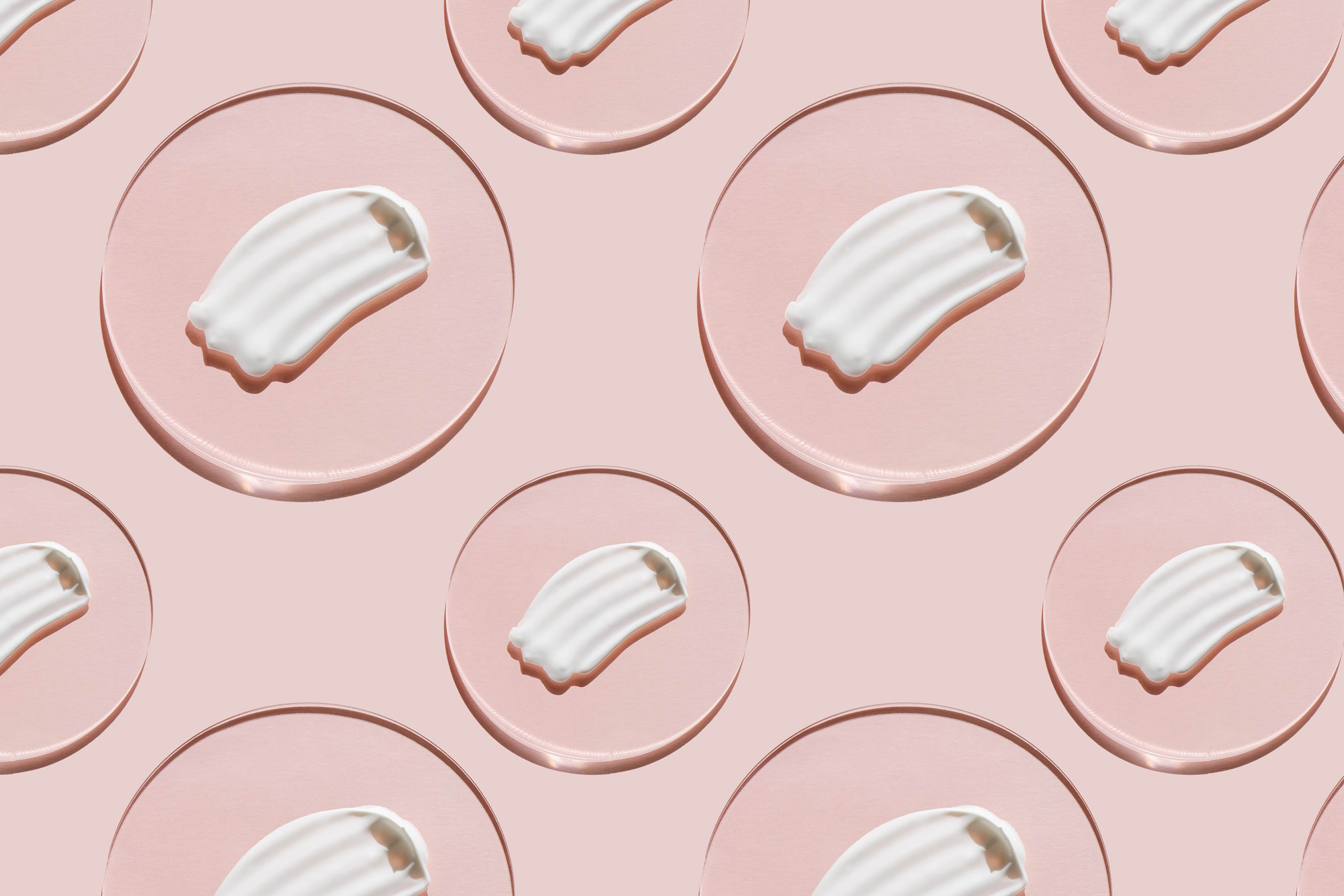 Repeating pattern of a white milky cream smear on a circular oil drop against a pink background.