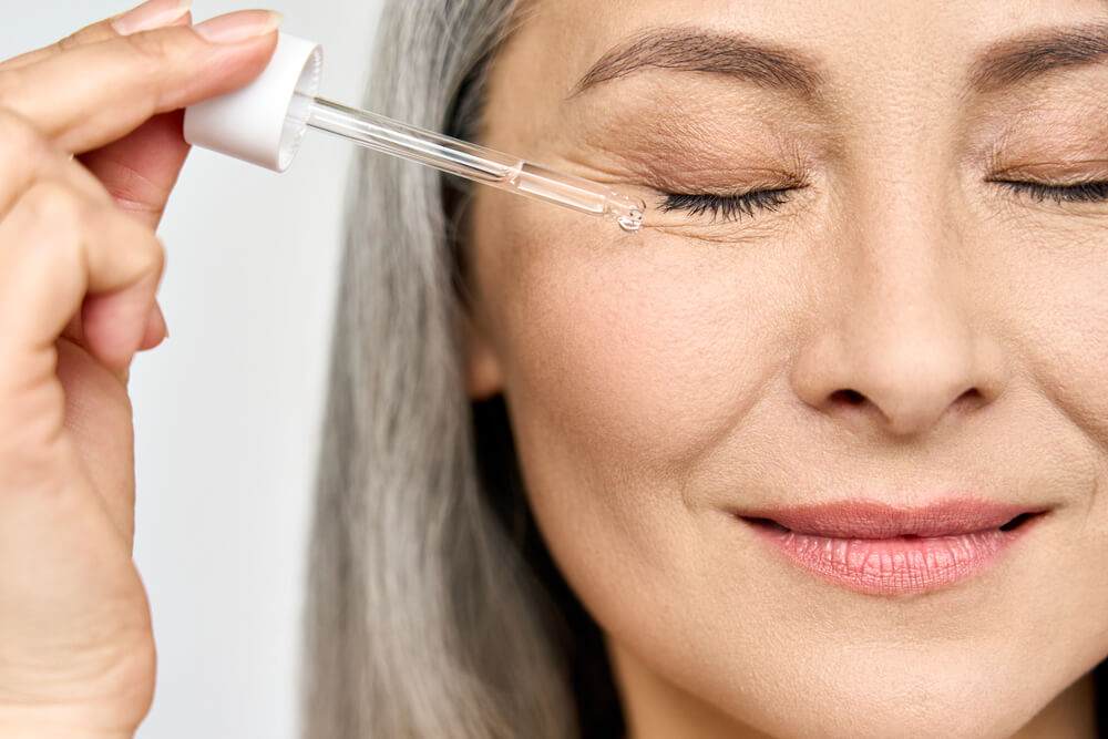 East asian woman applying serum to her face with a pipette