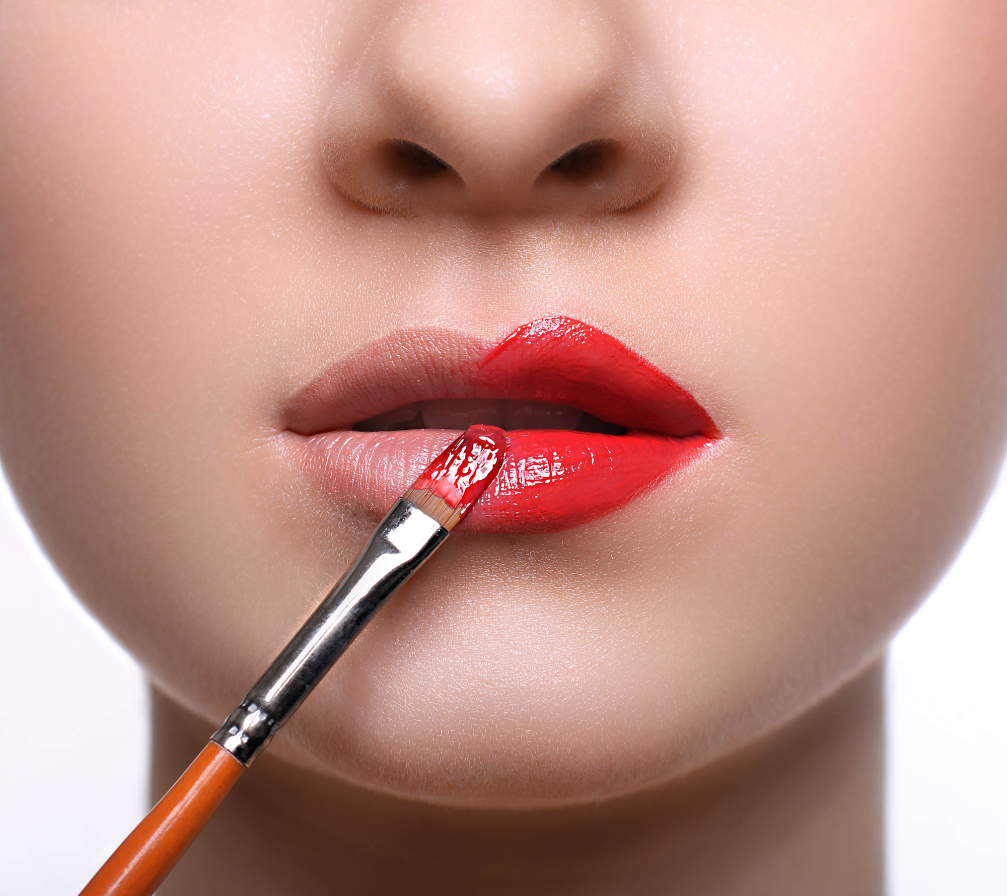 Cropped close-up on a young white woman's lips as she applies ruby red lip stain to her lips using a brush.