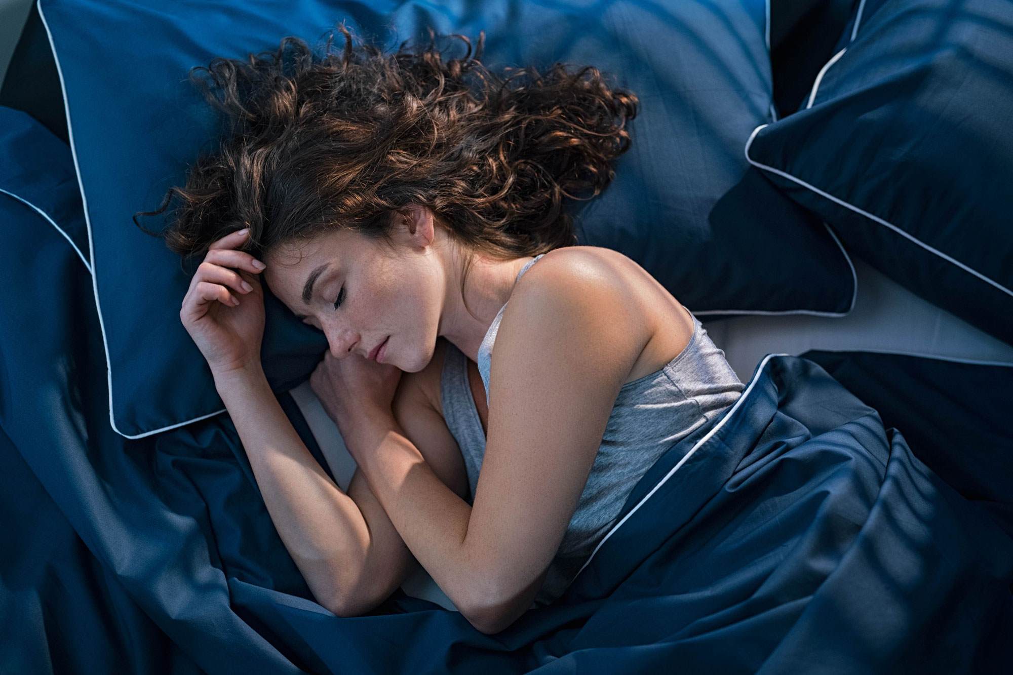 Young white woman with brown curly hair lying asleep in her bed.