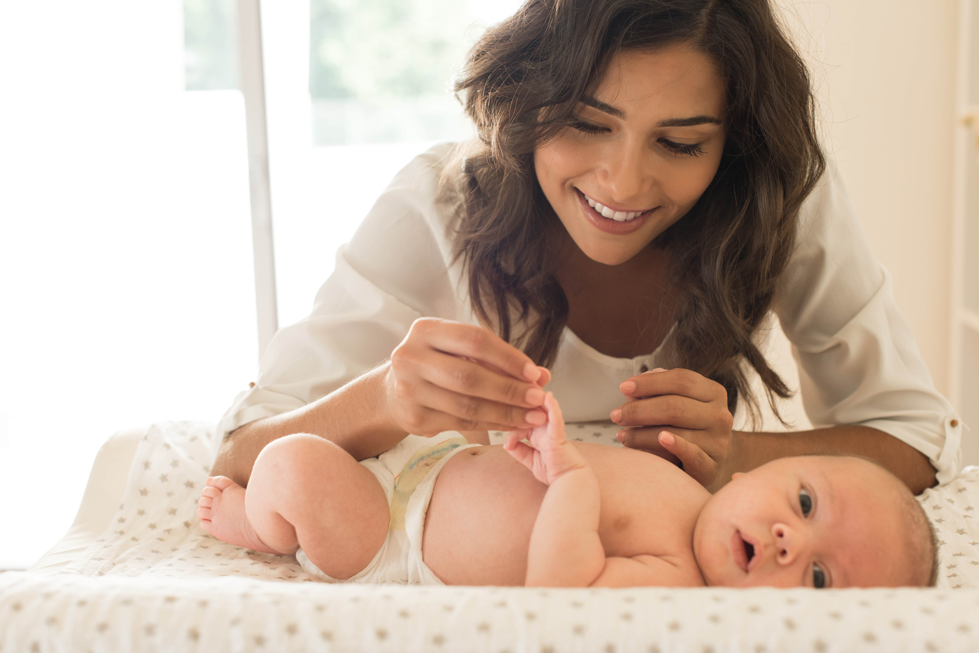 Young white woman with long brown straight hair playing with a baby who is lying on a changing mat,