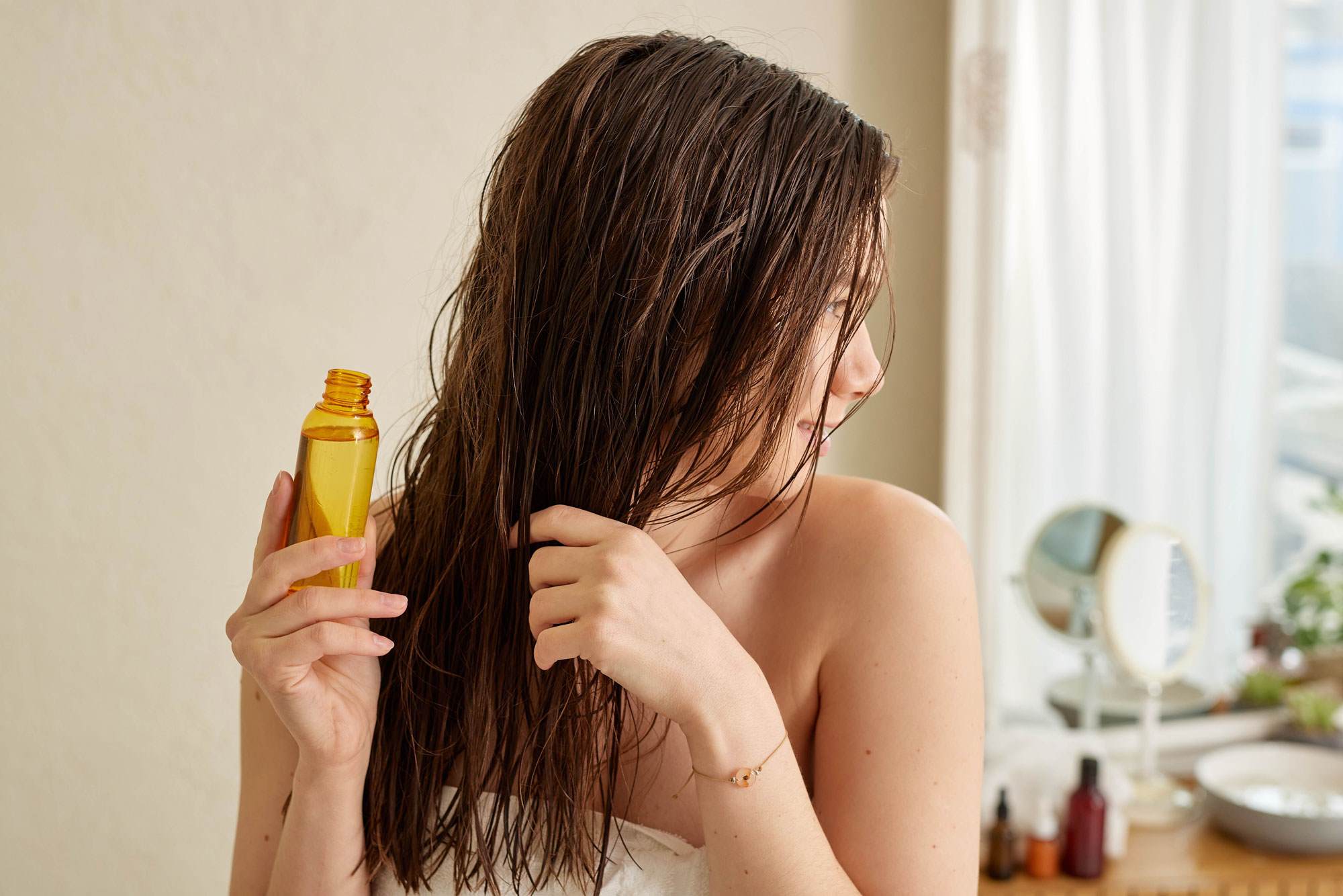Young white woman with wet brown hair. She is holding a bottle. Her hair covers her face.
