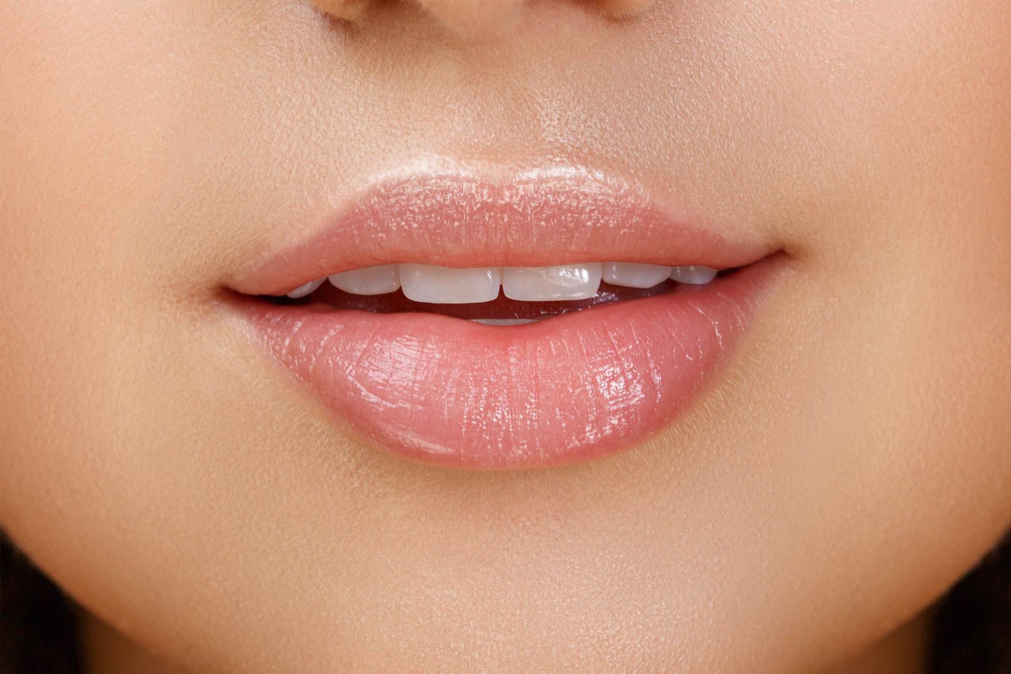 Cropped image of a smiling white woman with pink lips. The focus is on her beautiful smile.