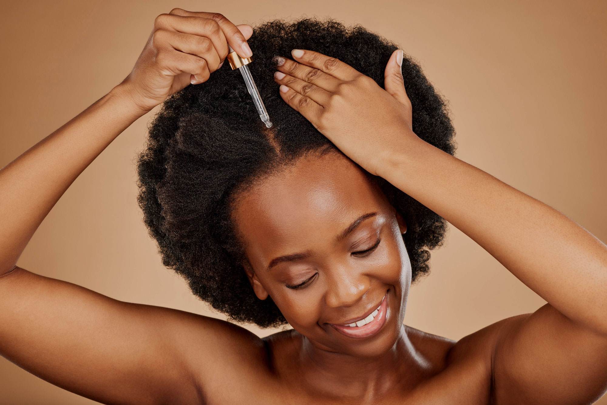Young black woman with black natural hair applying serum to her scalp.