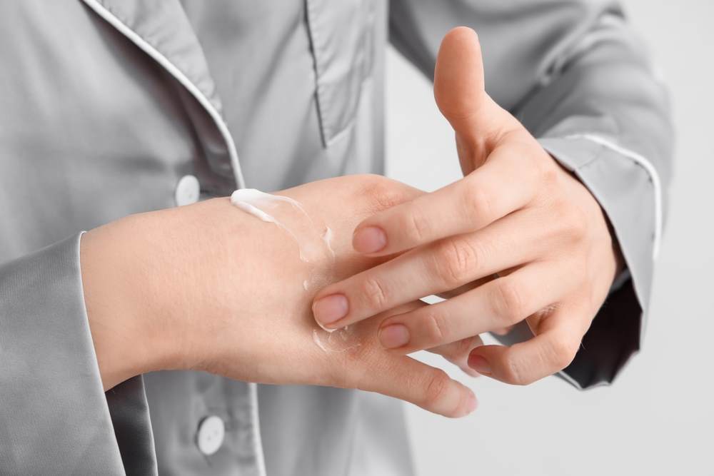 silky watery lotion close up on the hands of a young woman in silk pyjamas applying lotion