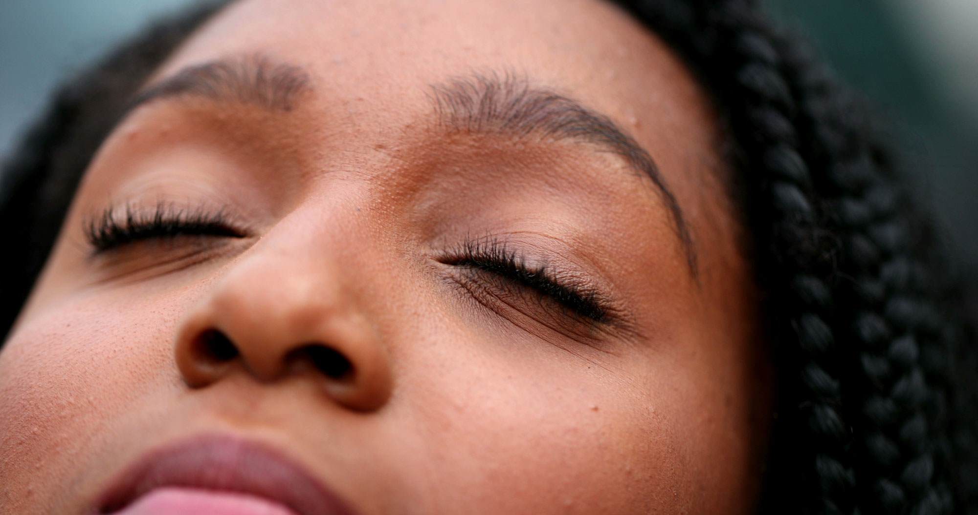 Young black woman with her eyes closed smiling and looking up.