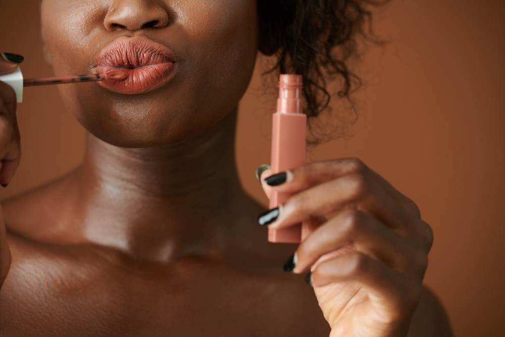 Cropped image showing the mouth of a young black woman applying the volumising lip stick