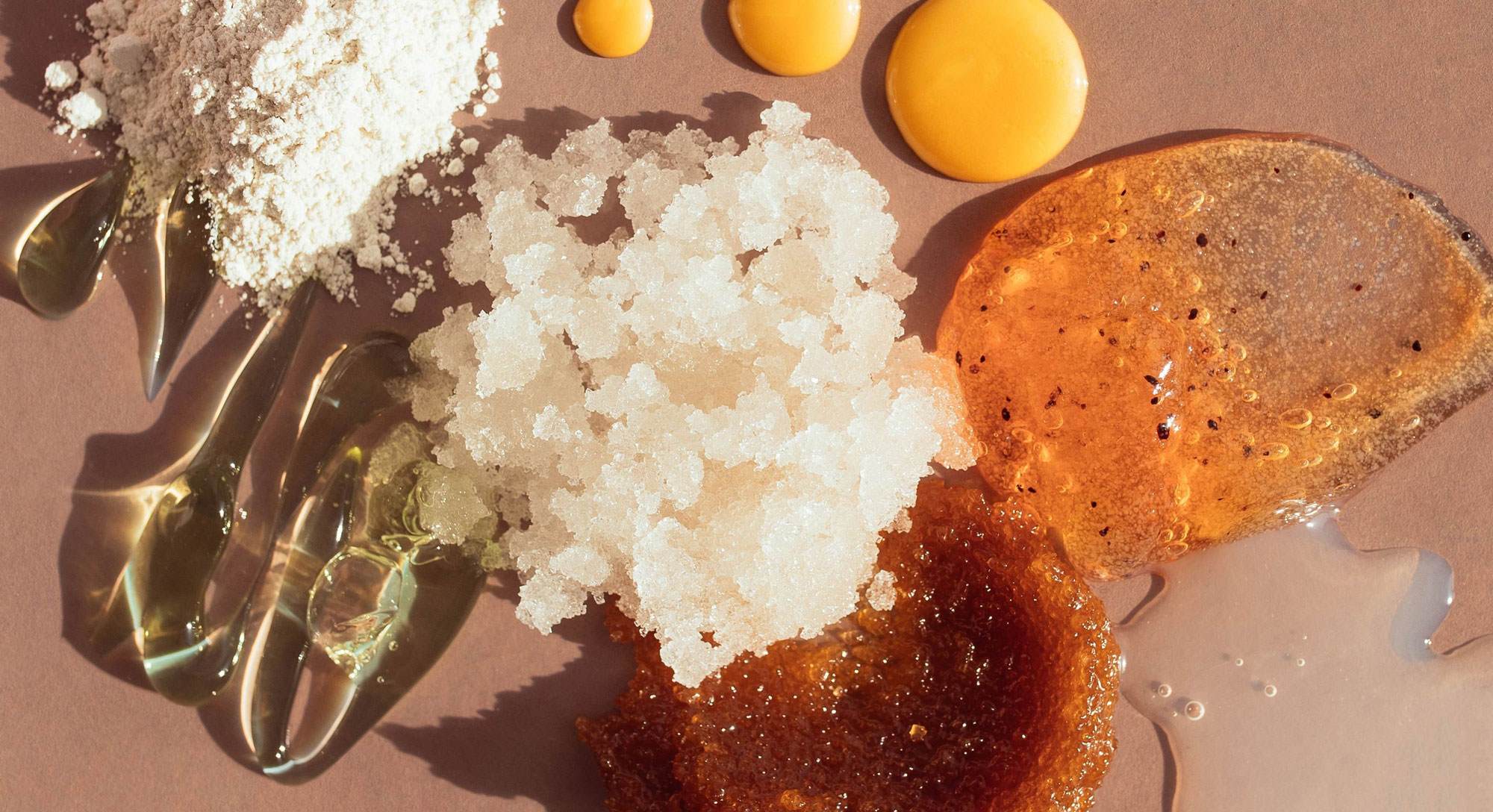 ピンクの背景に配置された、異なる質感の化粧品調合物の混合物