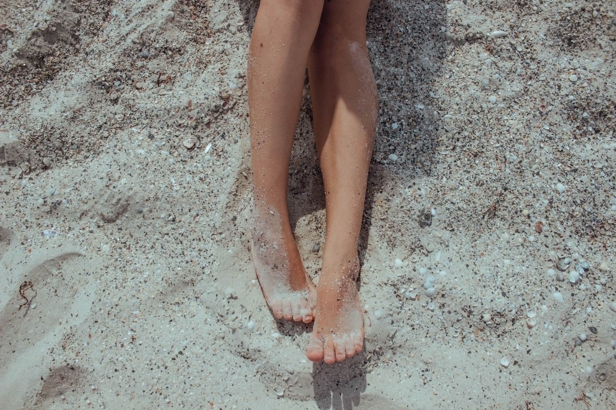 cropped image of a white womans legs on the beach covered in sand