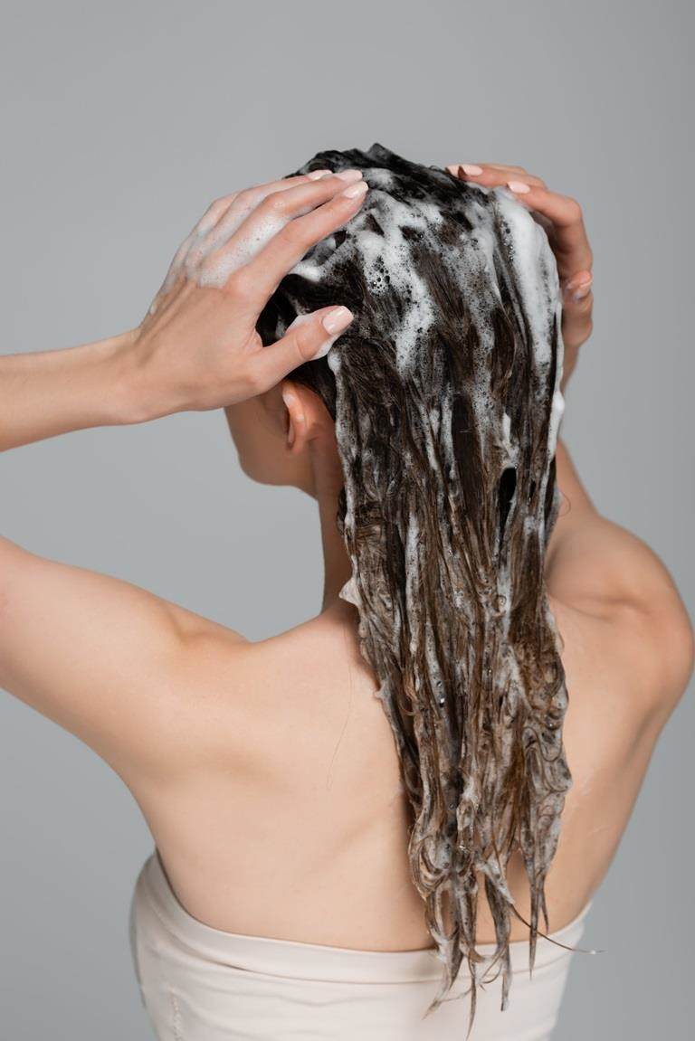 White woman washing her brown hair, photo is from behind.