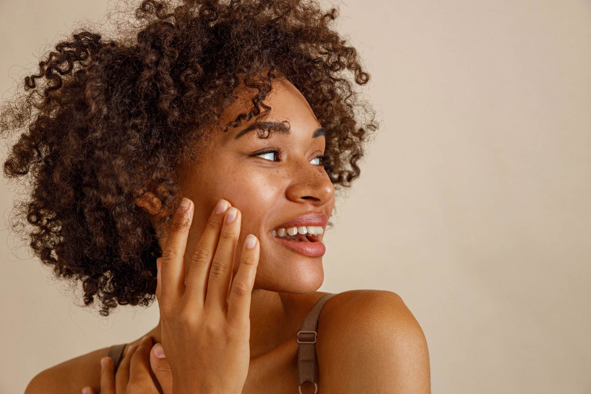 women with curly hair style posing against beige wall