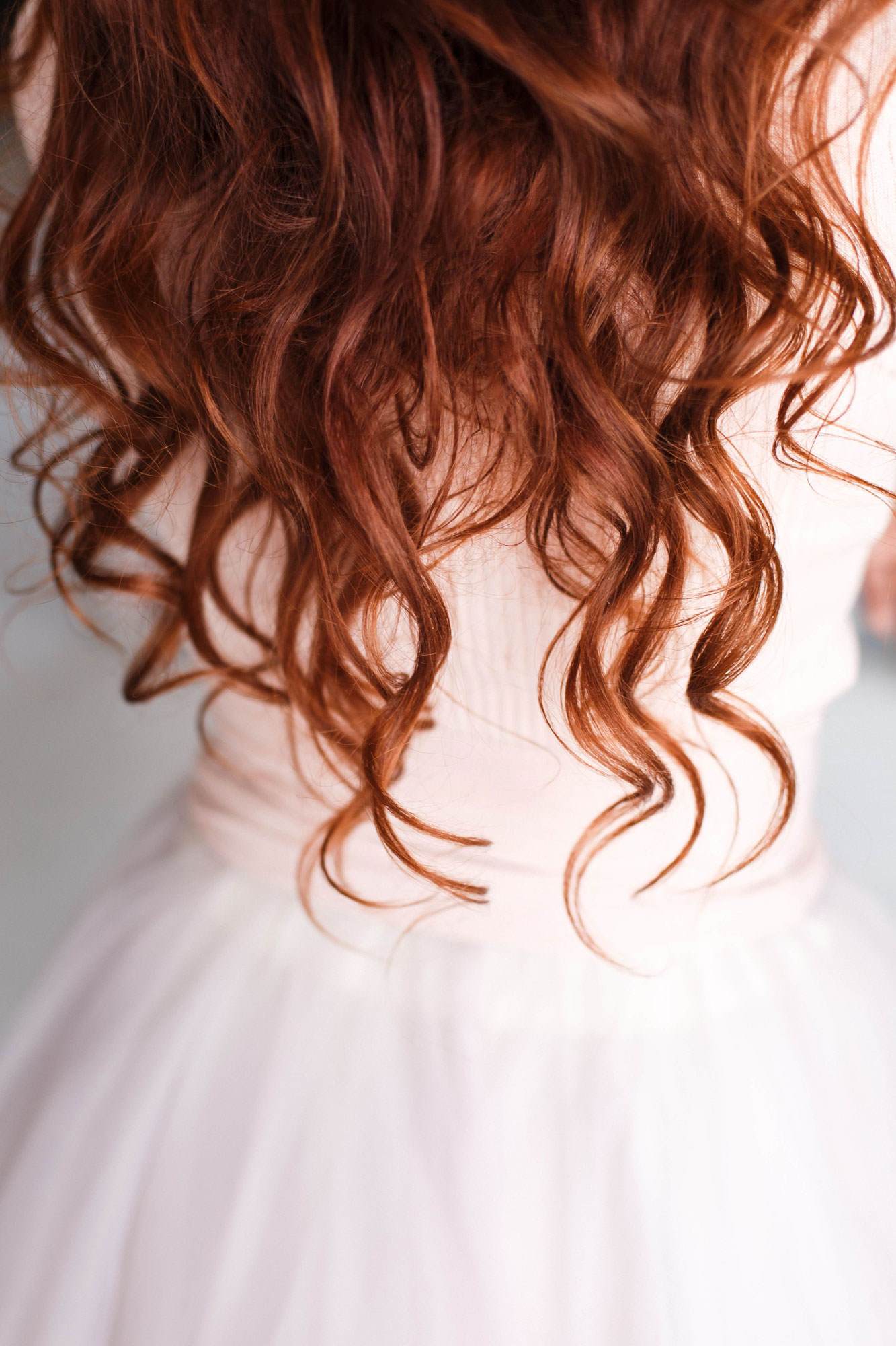 白いドレスを着た女性の背中を写したトリミング写真。波打つカールをした長い赤毛をしている。