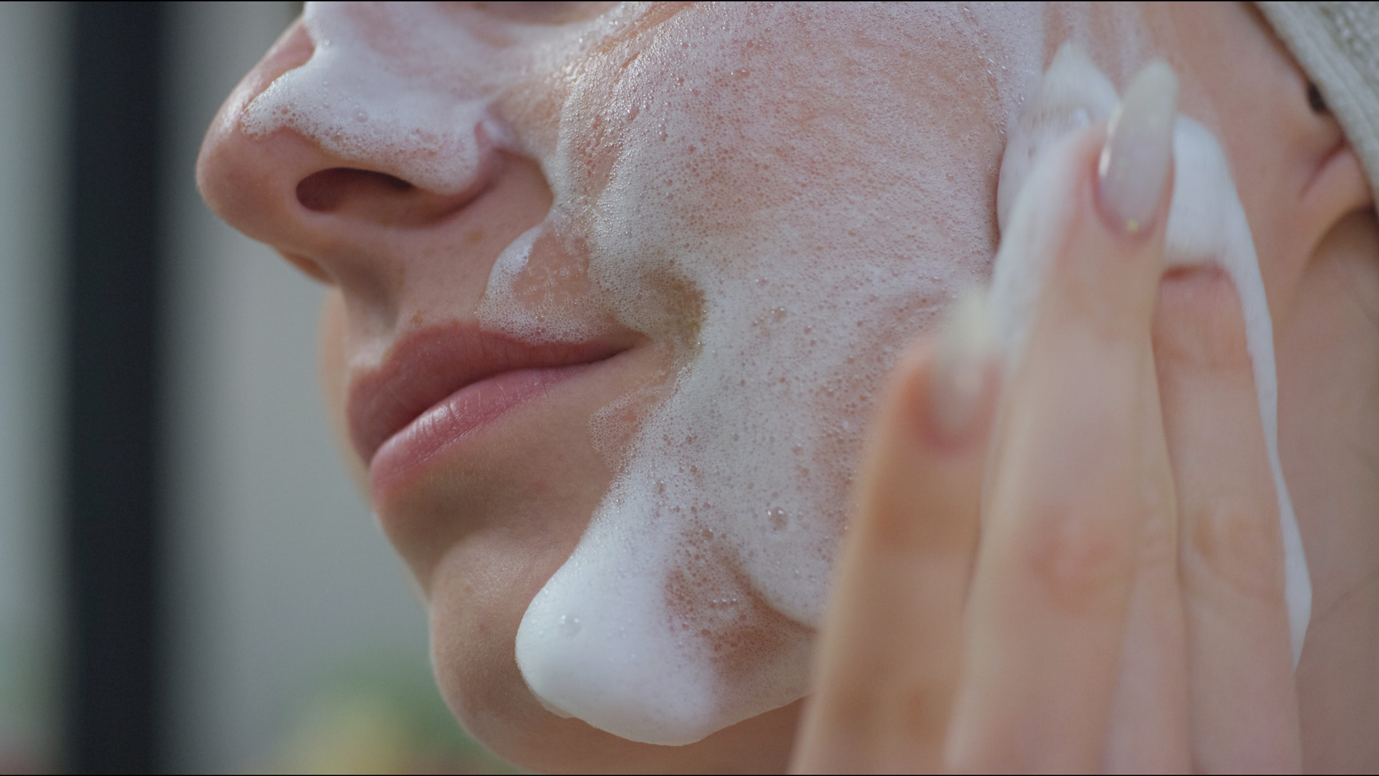 Cropped close up showing cheek of a white woman applying the infusion cream soft cleanser
