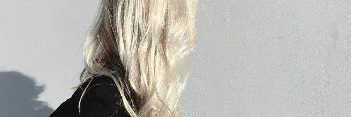 Photo of a blonde haired woman whose face is covered by her hair. The photo is taken from a high angle and she is in profile.